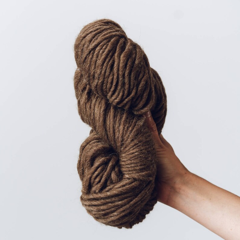 K&ouml;nnte beinhalten: Eine gro&szlig;e Kugel braunen Garns, die in einer Hand gehalten wird. Das Garn ist weich und flauschig und perfekt zum Stricken oder H&auml;keln.