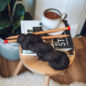 K&ouml;nnte beinhalten: Ein Holzhocker mit einem braunen Garnkn&auml;uel darauf. Das Garn ist dunkelgrau und hat eine nat&uuml;rliche Textur. Der Hocker steht auf einem wei&szlig;en, flauschigen Teppich. Ein Buch mit dem Text "creative space" liegt auf dem Hocker. Eine Tasse Kaffee steht auf dem Buch.