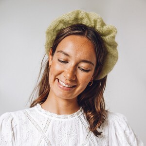 K&ouml;nnte beinhalten: Eine Frau mit braunen Haaren tr&auml;gt eine hellgr&uuml;ne Strickm&uuml;tze und ein wei&szlig;es Spitzenoberteil.