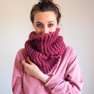 May include: A woman wearing a pink knitted cowl neck scarf. The scarf is thick and has a ribbed texture.