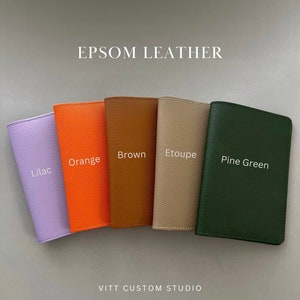 May include: Five rectangular passport holders made of textured Epsom leather arranged in a row. The colors from left to right are labeled as Lilac, Orange, Brown, Etoupe, and Pine Green. The text EPSOM LEATHER and VITT CUSTOM STUDIO are visible.