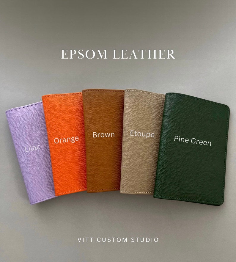 May include: Five rectangular passport holders made of textured Epsom leather arranged in a row. The colors from left to right are labeled as Lilac, Orange, Brown, Etoupe, and Pine Green. The text EPSOM LEATHER and VITT CUSTOM STUDIO are visible.