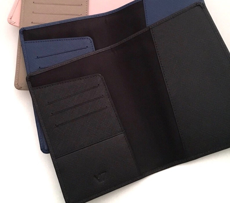 May include: Three open passport holders with a textured crosshatch finish. The front holder is black, the middle is navy blue, and the back is beige. Each holder features interior card slots and a pocket for documents, with a small logo embossed at the bottom.