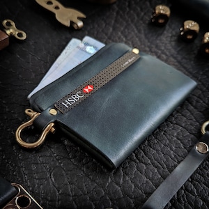 May include: A dark blue leather wallet with a brass hook and a card slot with a black and brown patterned insert. The card slot has the HSBC logo with a red star.