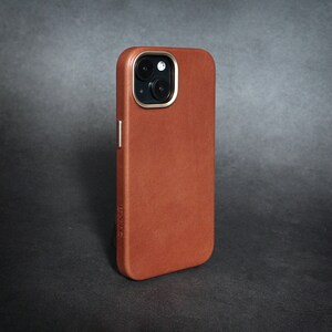May include: A brown leather phone case with a gold trim around the camera lens. The case has the word "DNC" embossed on the bottom.