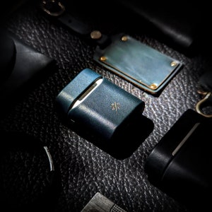 May include: A dark blue leather case with a subtle cross pattern and a gold accent. The case is made of high-quality leather and has a sleek, modern design.