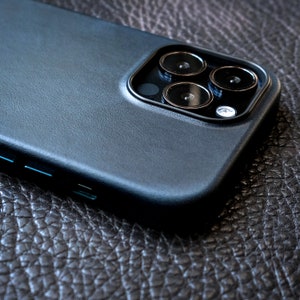 Pu&ograve; includere: Una custodia per telefono in pelle nera con un rialzo per la fotocamera. Il rialzo della fotocamera ha quattro obiettivi, di cui tre sono visibili nell'immagine.
