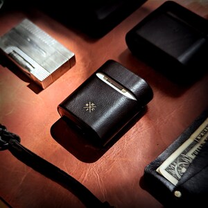 May include: A black leather case with a gold logo and a white interior. The case is sitting on a brown leather surface.