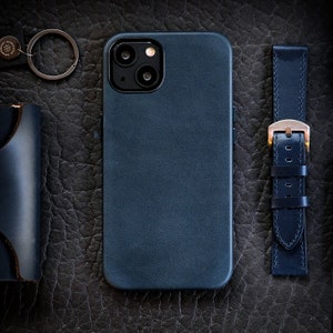 Pu&ograve; includere: Una custodia per telefono in pelle blu scuro con un ritaglio per l'obiettivo della fotocamera e una superficie testurizzata.