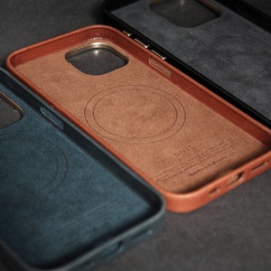 May include: Three phone cases in different colors: blue, brown, and black. Each case has a circular cutout for wireless charging and a gold trim around the edges.
