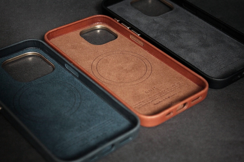 May include: Three phone cases in different colors: blue, brown, and black. Each case has a circular cutout for wireless charging and a gold trim around the edges.
