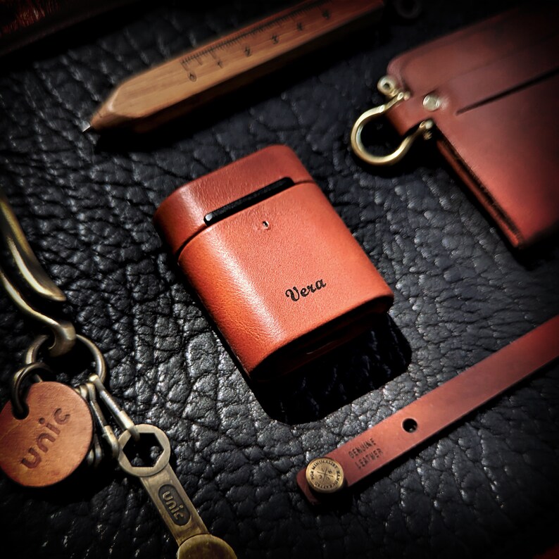 May include: A brown leather case with the word "Vera" embossed on the front. The case is sitting on a black leather surface.