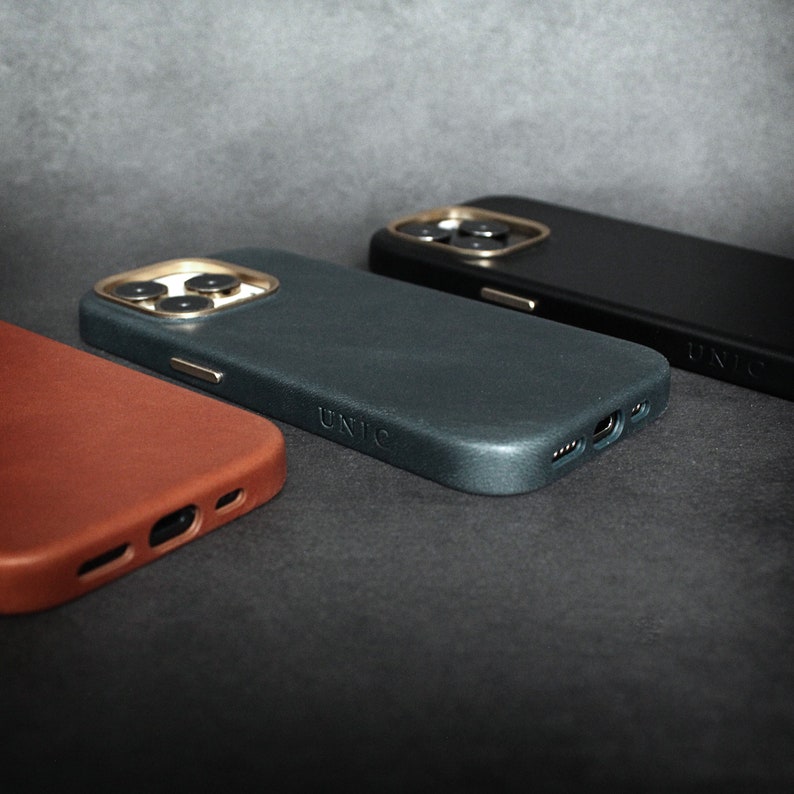 May include: Three phone cases in different colors: brown, dark blue, and black. Each case has a raised camera bump and the word "UNIC" printed on the side.
