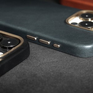 May include: Two phone cases with a dark blue and black color scheme. The cases have a gold trim around the camera lens and a textured surface.
