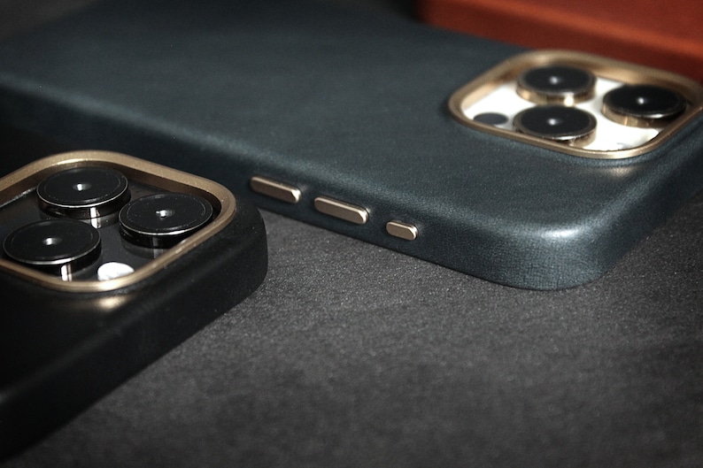 May include: Two phone cases with a dark blue and black color scheme. The cases have a gold trim around the camera lens and a textured surface.