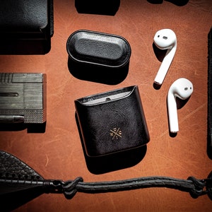 May include: A black leather case with a gold logo and a zipper closure. The case is open and contains two white wireless earbuds.