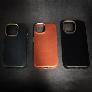 May include: Three phone cases, one black, one brown leather, and one dark blue. All cases have a gold ring around the camera lens.