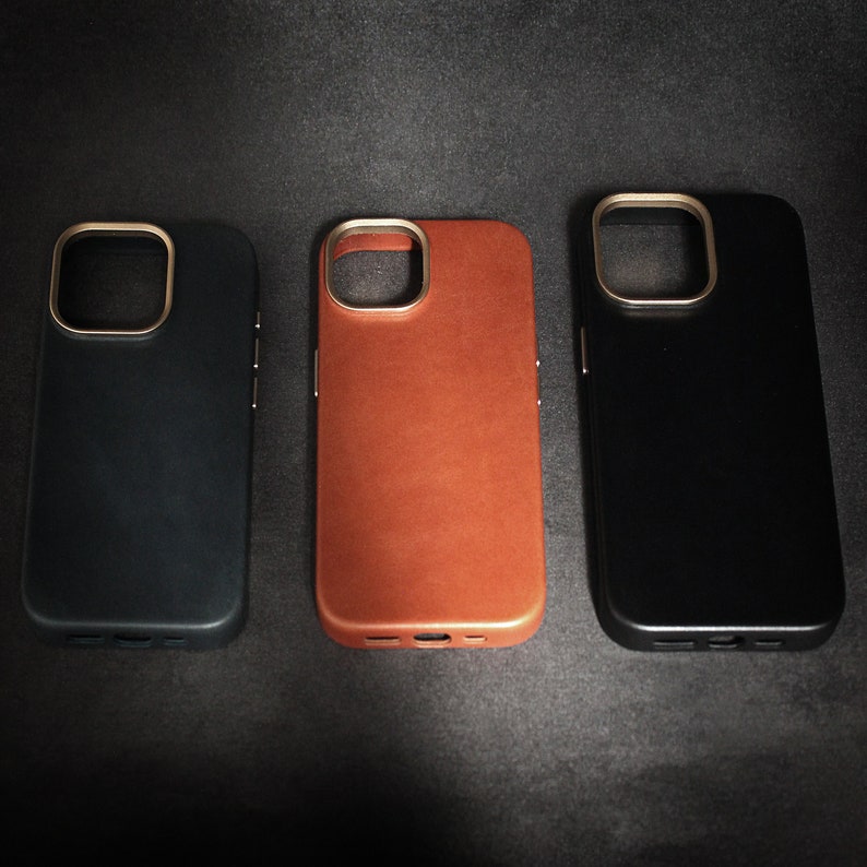 May include: Three phone cases, one black, one brown leather, and one dark blue. All cases have a gold ring around the camera lens.