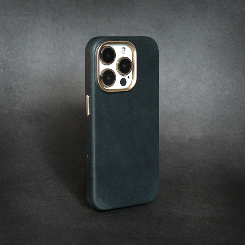 May include: A dark blue phone case with a gold trim around the camera lens. The case has a textured surface.