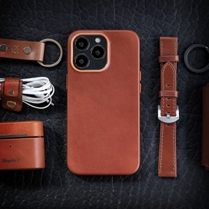 Pu&ograve; includere: Una custodia per telefono in pelle marrone con un ritaglio per l'obiettivo della fotocamera e un cinturino da orologio in pelle marrone con una fibbia argentata.