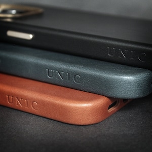 May include: Three leather phone cases stacked on top of each other. The top case is black, the middle case is dark blue, and the bottom case is brown. All three cases have the word "UNIC" embossed on them.