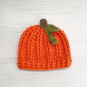 Puede incluir: Un gorro de ganchillo naranja con forma de calabaza, con costillas verticales y un tallo marr&oacute;n y detalles de hojas verdes. El gorro est&aacute; dise&ntilde;ado para parecerse a una calabaza, perfecto para el oto&ntilde;o o Halloween.