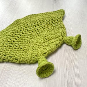 May include: A handmade, lime green crochet leaf-shaped item with two bell-shaped appendages. The item is made of thick yarn, with a textured surface and a pointed tip. The bell shapes are at the base of the leaf.