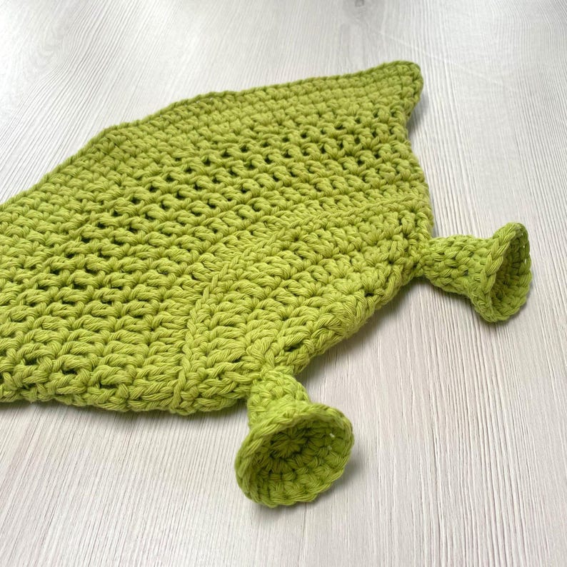 May include: A handmade, lime green crochet leaf-shaped item with two bell-shaped appendages. The item is made of thick yarn, with a textured surface and a pointed tip. The bell shapes are at the base of the leaf.