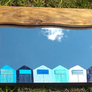 May include: A wooden framed mirror with a blue sky reflection. The bottom of the mirror has a painted design of beach huts in shades of blue, white, and black.
