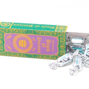 Peut inclure: Une boîte verte et dorée avec le texte "Book of Potions" sur le devant. La boîte est ouverte et contient des bonbons enveloppés d'argent.
