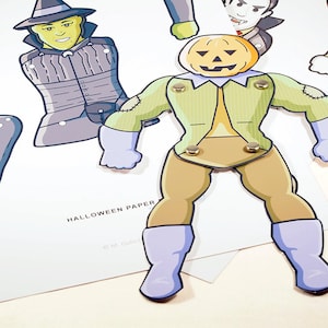 May include: A paper doll set with three characters: a witch, a vampire, and a Frankenstein-like monster with a pumpkin head. The characters are all wearing costumes and have different facial expressions. The paper doll set is titled "Halloween Paper" and is copyright M. Cullen.