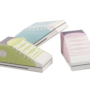 May include: Three paper shoe boxes in the shape of high-top sneakers. The boxes are decorated with a white and light blue stripe pattern, a white and green stripe pattern, and a white and pink stripe pattern.