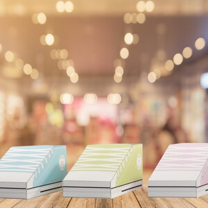 May include: Three shoe-shaped boxes made of cardboard. The boxes are in the colors blue, green, and pink. The boxes are sitting on a wooden surface.