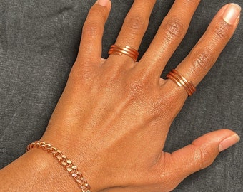 May include: A person's hand wearing three copper rings and a copper chain bracelet.