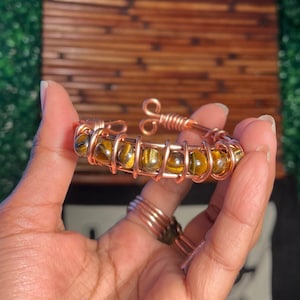 May include: A copper wire wrapped bracelet with tiger's eye beads. The bracelet is a warm copper color and the beads are a mix of brown and gold.