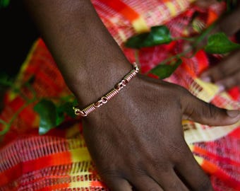 May include: A copper bracelet with a twisted wire design. The bracelet is worn on a person's wrist.