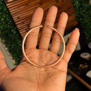 May include: A simple, rose gold bangle bracelet. The bracelet is round and smooth, with a polished finish.