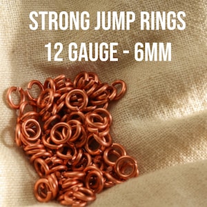 Könnte beinhalten: Ein Haufen Kupfer-Sprünge, 12 Gauge und 6 mm groß. STRONG JUMP RINGS 12 GAUGE - 6MM ist in weißer Schrift auf einem beigefarbenen Stoffhintergrund geschrieben.