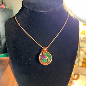 Könnte beinhalten: Eine goldene Kettenkette mit einem Anhänger aus grünem und rosafarbenem Edelstein, der mit Kupferdraht umwickelt ist.