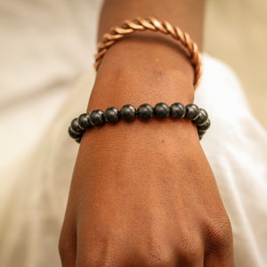 May include: A black beaded bracelet on a person's wrist. The bracelet is made of round, black beads.