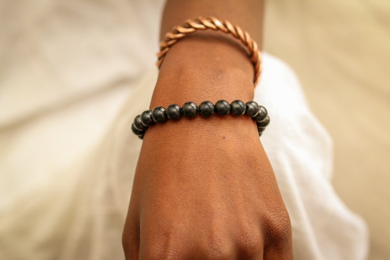 May include: A black beaded bracelet on a person's wrist. The bracelet is made of round, black beads.