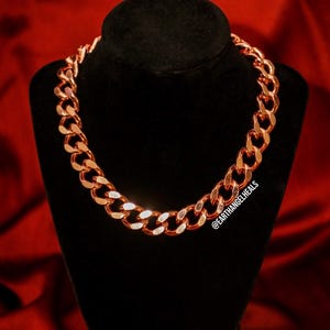 May include: A 16mm Cuban link chain made of pure solid copper. The chain is displayed on a black velvet stand against a red background. The chain is a bright copper color.