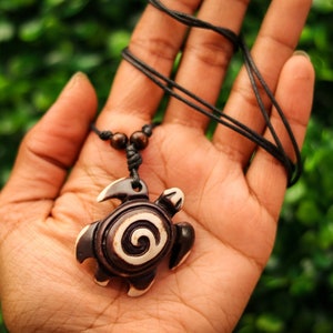 May include: A brown and white wooden turtle pendant necklace with a black cord. The turtle has a spiral design on its shell.