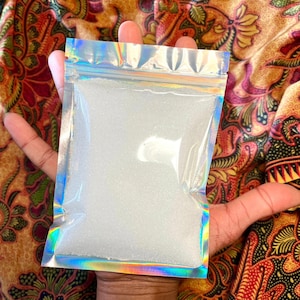 以下が含まれることがあります： 白い虹色のグリッターで満たされた透明なプラスチック製の再封可能なバッグ