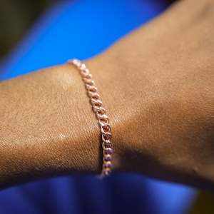 May include: A close-up of a person's arm wearing a rose gold chain bracelet.