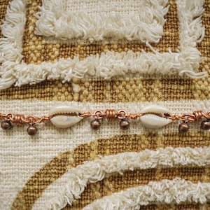May include: A copper wire bracelet with white seashells and copper beads.