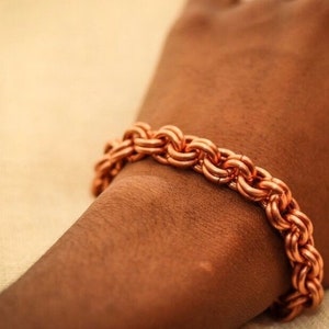 May include: A copper bracelet with a braided design. The bracelet is worn on a person's wrist.