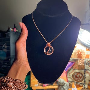 May include: A copper wire wrapped necklace with a black gemstone pendant. The pendant is a sphere with a copper wire design.