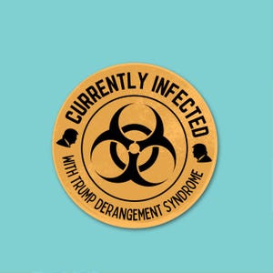May include: A round, gold-colored sticker with black text and graphics. The text reads "CURRENTLY INFECTED" and "WITH TRUMP DERANGEMENT SYNDROME" around a black biohazard symbol. Silhouettes of a person's profile are on either side.