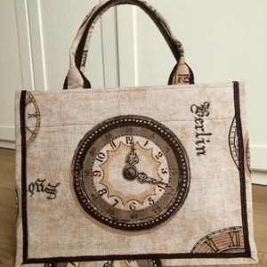 May include: A beige canvas tote bag with brown trim and a repeating pattern of vintage clocks. The bag has a brown leather handle and the word "Berlin" is printed on the side.